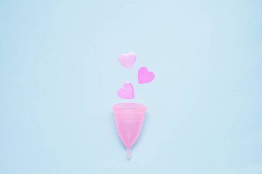 Pembe kalpli regl kupası regl dönemini sembolize ediyor. Üst görünüm, açık mavi arkaplan.