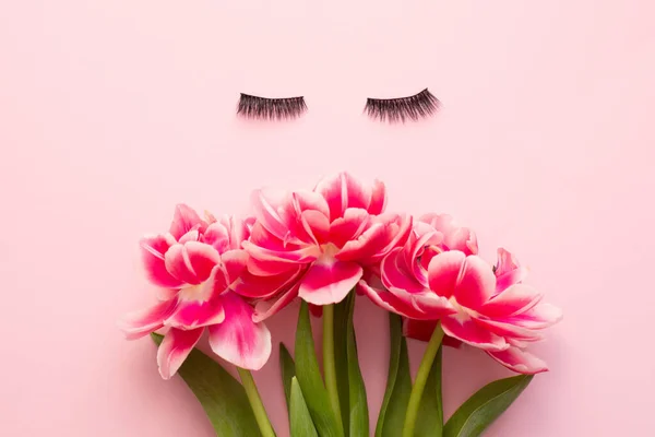 False eyelashes extensions black on pink background with bright flowers, top view. Beauty concept.