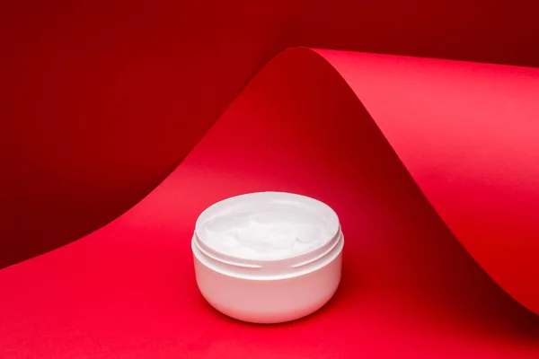 jar of beauty cream on red wave paper background