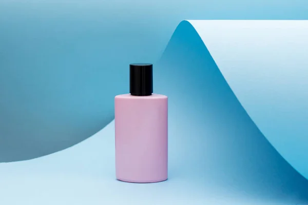 Mavi kağıdın üzerinde duran parfüm kokusu. pembe şişe, modern güzellik eğilimi