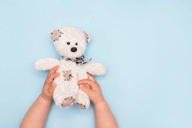 İki çocuk eli mavi arka planda küçük bir oyuncak ayı tutuyor.