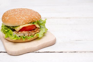 Beyaz ahşap arka planda sığır etli, domatesli ve peynirli leziz bir burger.