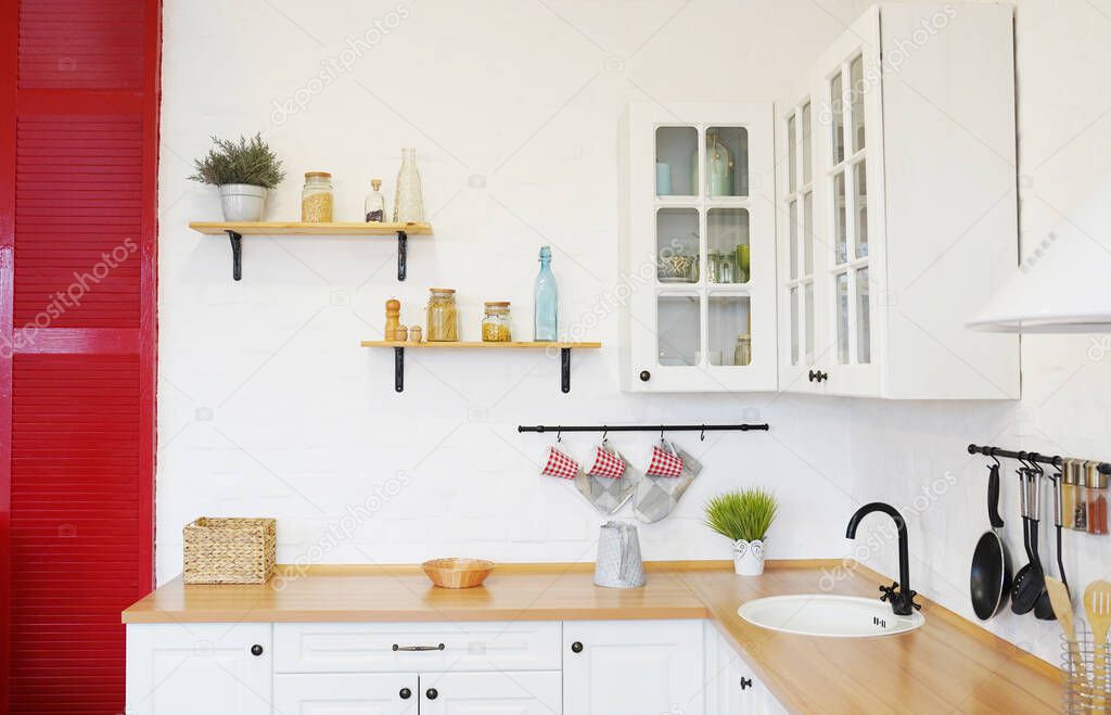 Modern new light interior of kitchen with white furniture, white brick wall and different cute jars on the shelves.