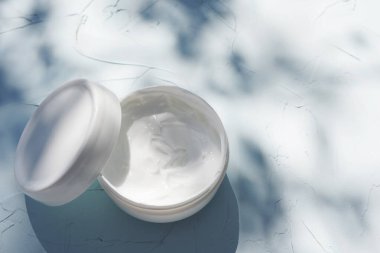 Mavi arka planda, tropikal bir bitkinin gölgesi olan krem. Eko kozmetik kavramı, kopyalama alanı