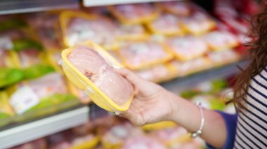 Yiyecek dükkanında et. Kadın süpermarkette paketlenmiş taze tavuk eti seçiyor. .