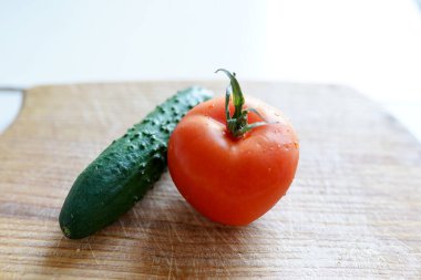 Beyaz arka planda tahta kesen kırmızı domates ve yeşil salatalık. Uzayı kopyala Pişirmek için taze domates. Bir damla su sebzeli domates.