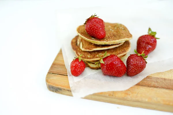 Plate full of fluffy golden pancakes with strawberries on the wooden board