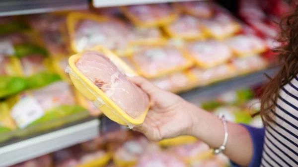 Yiyecek dükkanında et. Kadın süpermarkette paketlenmiş taze tavuk eti seçiyor. .