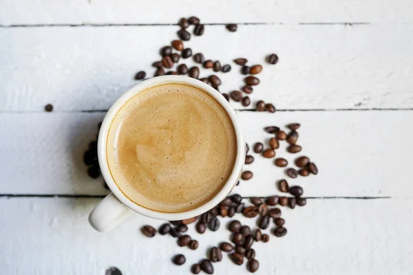 白い木の背景にコーヒー豆とコーヒーのカップ — ストック写真