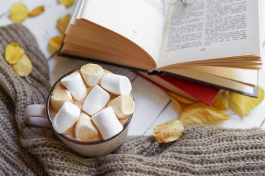 Ahşap zemin üzerinde sonbahar yaprakları olan sıcak kahve ve kitap - mevsimsel rahatlama kavramı