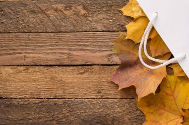 Ahşap zemin üzerinde sonbahar sarısı kurumuş yapraklar olan beyaz paket, kopyalama alanı. sonbahar indirimi