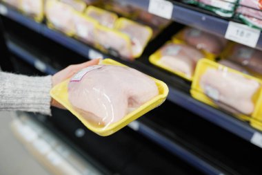 Kadın markette paketlenmiş tavuk eti seçiyor.