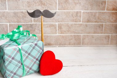 Kağıt ambalajlı hediye kutusu, bıyıklı etiket kartı, tahta arka planda kırmızı kalp, üst manzara, Babalar Günü konsepti.