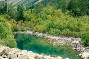 A green rocky lake and a forest in foggy Caucasus mountains of Russia