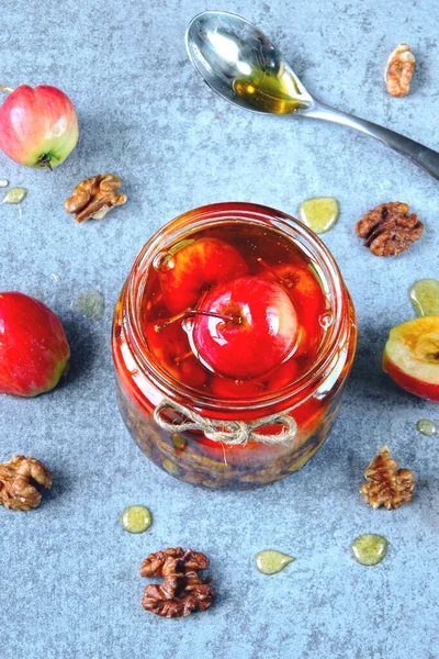 Paradise apples and walnuts in honey. A jar of honey with small apples and nuts. Nutritious honey mixture in the jar. Vitamin mixture of honey, apples and nuts.