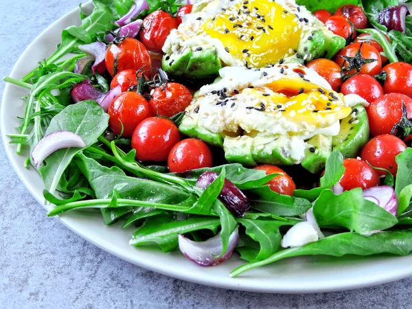 Bir tabakta yumurta, roka ve kiraz domatesli avokado. Tabak ve sağlıklı bir yemek. Avokado, yumurta, roka ve vişneli domatesli sağlıklı bir salata. Sağlıklı yemek..