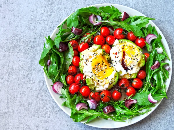 Avocado with egg, arugula and cherry tomatoes on a plate. Plate with a healthy meal. A healthy healthy salad with avocado, egg, arugula and cherry tomatoes. Healthy food.