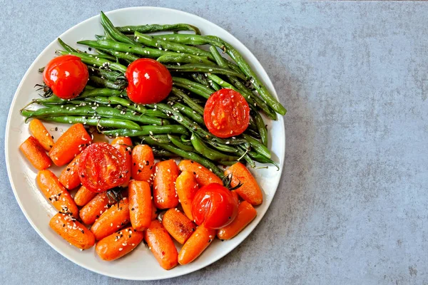 Healthy food on a plate. Green string beans and baby carrots, cooked on the grill. Vegan lunch. Useful salad of green beans and carrots. Green beans and carrots.