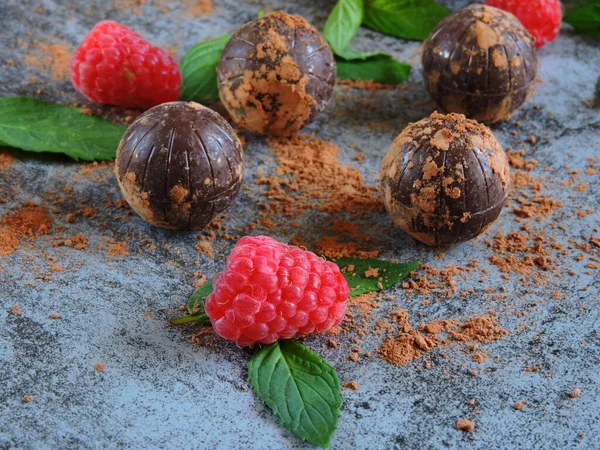 Chocolate truffle, raspberry and mint. Chocolate balls with raspberry decoration. Dark chocolate truffle mint raspberry. The concept of a chocolate-raspberry dessert. Chocolate truffles and ripe raspberries. Fresh bright mint.