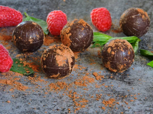 Chocolate truffle, raspberry and mint. Chocolate balls with raspberry decoration. Dark chocolate truffle mint raspberry. The concept of a chocolate-raspberry dessert. Chocolate truffles and ripe raspberries. Fresh bright mint.