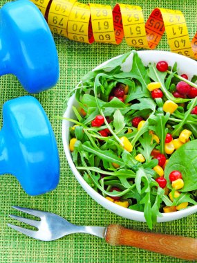 Beyaz kasede roka, mısır ve inek üzümü salatası. Dambıllar ve mezura. Kilo kaybı ve beslenme kavramı. Lezzetli ve sağlıklı diyet salatası.