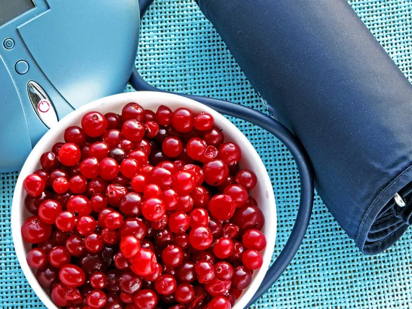 Cranberries in a white dish and the blood pressure measurement apparatus. The concept of utility cranberry for the cardiovascular system.
