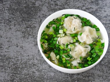 Çorbalı hamur tatlısı ve beyaz bir kasede otlar. Yemek çubukları. Çin usulü etli börek..