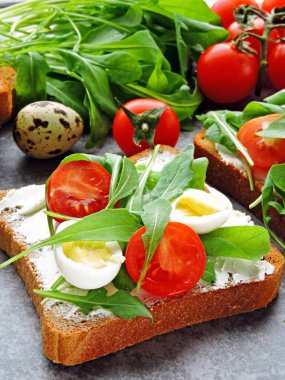 Buğday ekmekli tost roka, bıldırcın yumurtası ve vişneli domates. Faydalı atıştırmalık konsepti. Atıştırmalık bir şeyler. Parlak, lezzetli ve sağlıklı sağlık kadehleri. Roka ve krem peynirli sandviç.