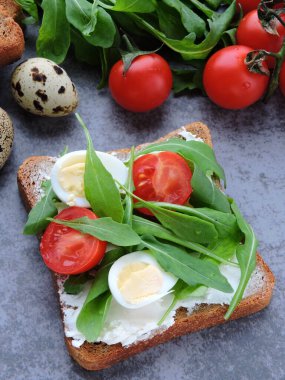 Buğday ekmekli tost roka, bıldırcın yumurtası ve vişneli domates. Faydalı atıştırmalık konsepti. Atıştırmalık bir şeyler. Parlak, lezzetli ve sağlıklı sağlık kadehleri. Roka ve krem peynirli sandviç.