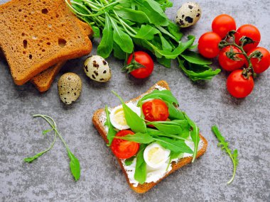 Buğday ekmekli tost roka, bıldırcın yumurtası ve vişneli domates. Faydalı atıştırmalık konsepti. Atıştırmalık bir şeyler. Parlak, lezzetli ve sağlıklı sağlık kadehleri. Roka ve krem peynirli sandviç.