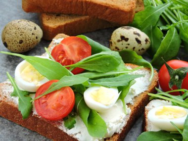 Buğday ekmekli tost roka, bıldırcın yumurtası ve vişneli domates. Faydalı atıştırmalık konsepti. Atıştırmalık bir şeyler. Parlak, lezzetli ve sağlıklı sağlık kadehleri. Roka ve krem peynirli sandviç.