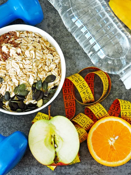 Fitness food concept. Oatmeal, fruits, nuts, seeds. Dumbbells and measuring tape. Proper nutrition and fitness for health and weight loss concept.