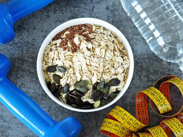 Fitness food concept. Oatmeal, fruits, nuts, seeds. Dumbbells and measuring tape. Proper nutrition and fitness for health and weight loss concept.