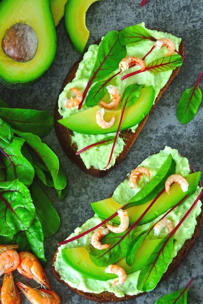 Toasts with avocado paste, prawns and chard. Healthy eating. Useful vegetarian open sandwiches with avocado and shrimp. Salad chard. Vegetarian foods. Superfoods.