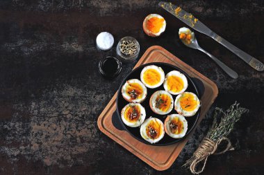 Yumuşak kaynamış yumurtalar dökme demir tavada yarıya iniyor. Bitki ve susamlı haşlanmış yumurta. Keto kahvaltısı ya da atıştırmalık. Düz yatıyordu.