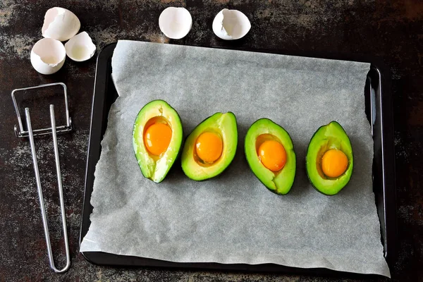 Raw egg in avocado on a baking sheet. Cooking avocado with egg. Keto lunch recipe.
