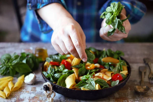 Hands of a chef with basil for cooking Italian pasta. Cooking one pan pasta. Hands of the chef mix the pasta in a pan. Vegan pasta with basil. Selective focus. Macro.