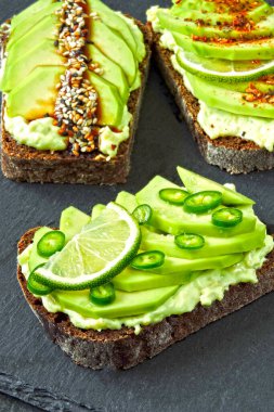 Lezzetli malzemelerle kaplanmış avokado tostu. Avokado tostları servis için gri bir tahtada sunuluyor..