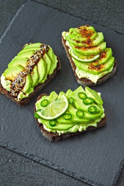 Lezzetli malzemelerle kaplanmış avokado tostu. Avokado tostları servis için gri bir tahtada sunuluyor..
