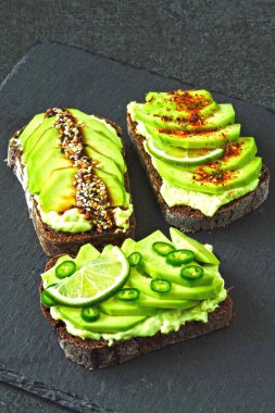 Lezzetli malzemelerle kaplanmış avokado tostu. Avokado tostları servis için gri bir tahtada sunuluyor..