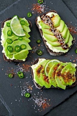 Lezzetli malzemelerle kaplanmış avokado tostu. Avokado tostları servis için gri bir tahtada sunuluyor..