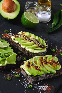 Lezzetli malzemelerle kaplanmış avokado tostu. Avokado tostları servis için gri bir tahtada sunuluyor..