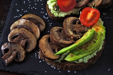 Mantarlı ve kiraz domatesli sağlıklı avokado tostları. Keto diyeti. Lezzetli malzemelerle kaplanmış avokado tostu..