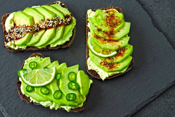 Beautifully plated avocado toast with delicious-looking toppings. Avocado toasts presented on a gray slate board for serving.