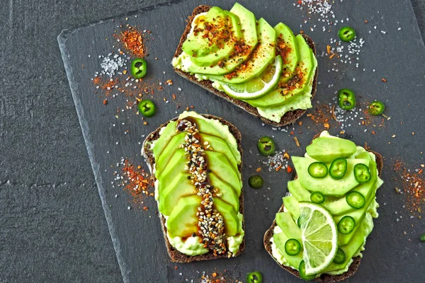 Beautifully plated avocado toast with delicious-looking toppings. Avocado toasts presented on a gray slate board for serving.
