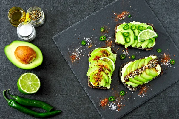 Beautifully plated avocado toast with delicious-looking toppings. Avocado toasts presented on a gray slate board for serving.