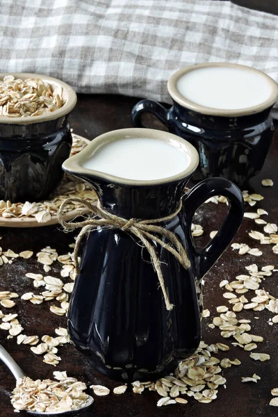 Oat milk in a milk jug on the background of oatmeal. Vegan milk. Eco food.