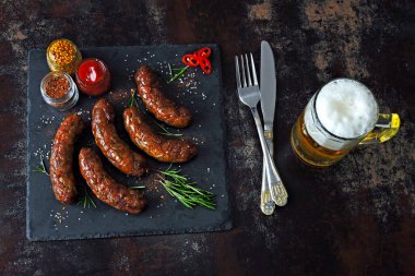 Koyu taştan bir tahtanın üzerinde ızgara sosis ve bir bardak bira. Baharatlı lezzetli kızarmış Bavyera sosisi. Münih sosisleri barbekü.