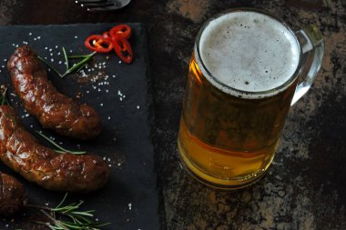 Koyu taştan bir tahtanın üzerinde ızgara sosis ve bir bardak bira. Baharatlı lezzetli kızarmış Bavyera sosisi. Münih sosisleri barbekü.