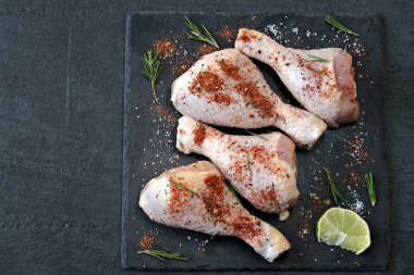 Koyu taş bir tahtanın üzerinde marine edilmiş çiğ tavuk bacağı..